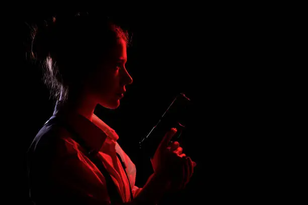 young woman with gun in dark with back red light. Profile silhouette view