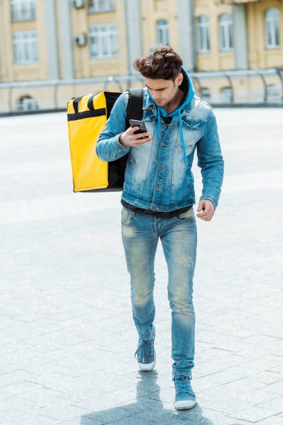 istock Handsome courier with thermo bag using cellphone while walking on urban street 1250675949