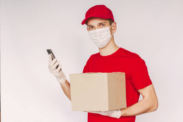 istock Young delivery guy in red uniform use mobile phone and carry parcel box in hand 1250676867