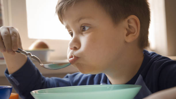istock Preschooler eats soup himself. Boy with full cheeks eats sitting at domestic kitchen table. Healthy food concept. Close up shot 1250676934