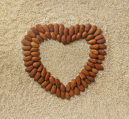 Floral composition: heart shape from almonds on background from sesame