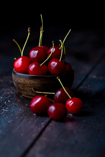 Fresh sweet cherries in a small bowl on dark wooden background with selective focus