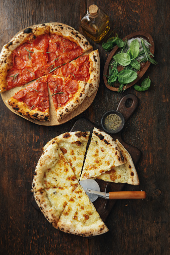 Italian Pepperoni Pizza and Four Cheese Pizza. Flat lay top-down composition on dark wooden background.