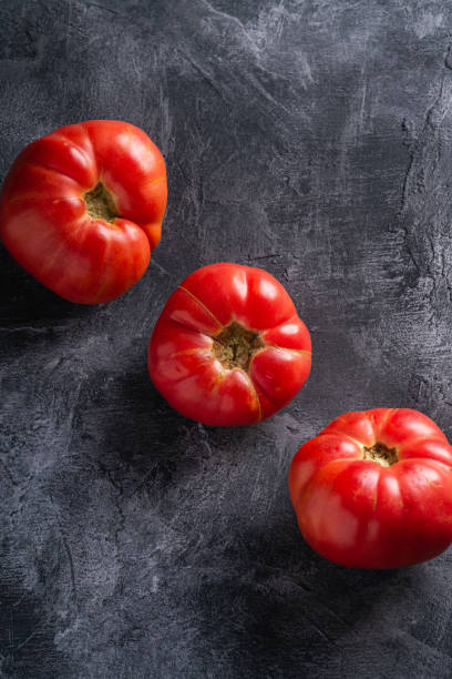 drei rosa erbstück tomatengemüse in reihe, frische rote reife tomaten, vegane lebensmittel, dunklen stein beton hintergrund, winkelansicht - tomato beefsteak tomato heirloom tomato pink stock-fotos und bilder