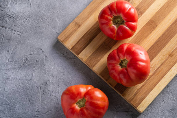 trois légumes roses de tomate d’héritage, tomates mûres rouges fraîches sur la planche de découpage en bois, nourriture végétalienne, fond en béton de pierre, vue supérieure - tomato beefsteak tomato heirloom tomato pink photos et images de collection