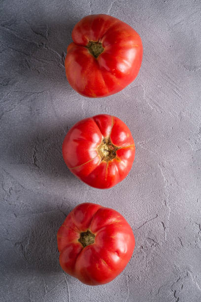 drei rosa erbstück tomatengemüse in reihe, frische rote reife tomaten, vegane lebensmittel, stein beton hintergrund, top-ansicht - tomato beefsteak tomato heirloom tomato pink stock-fotos und bilder