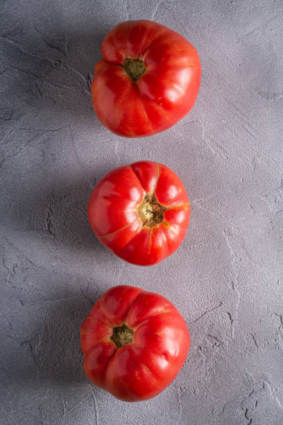 tres verduras de tomate de reliquia rosa en la fila, tomates maduros rojos frescos, comida vegana, fondo de hormigón piedra, vista superior - tomato beefsteak tomato heirloom tomato pink fotografías e imágenes de stock