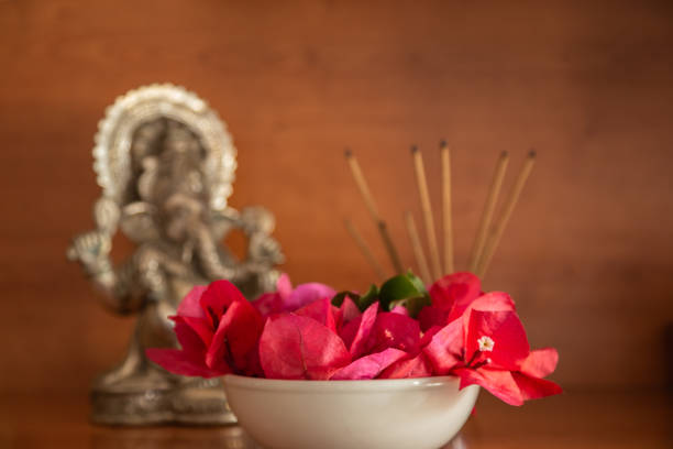 bowl with bougainvilleas and incense sticks and a statuette of god Ganesha blurred in the background
