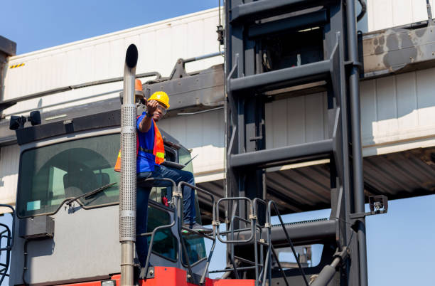istock Worker man in hardhat and safety vest holding laptop standing on container stackers control loading containers box from cargo 1250697024