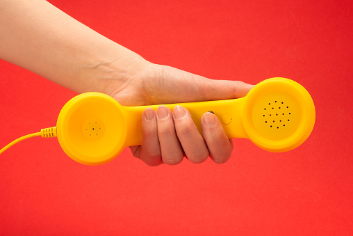 Yellow handset on a red background in woman hand. Copy space.