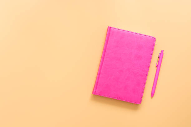 istock Pink notebook and ballpoint pen on a pastel yellow background. Top view, flat lay, copy space. 1250705153
