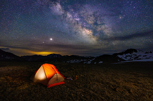 Backpacking Tent Glowing Under Night Sky and Milky Way - Outdoors adventure with glowing orange tent with sky full of stars and crisp Milky Way Galaxy. Colorado Rocky Mountains, Aspen, Colorado USA.