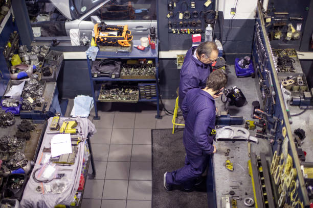 A senior man and his apprentice working on engine components. a Father and son wearing overalls working together on engine components in an automotive workshop. car mechanic top view stock pictures, royalty-free photos & images