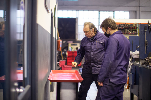 a Father and son wearing overalls working together on engine components in an automotive workshop.