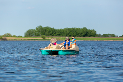 Three young children (two sisters and their little brother) in a paddle boat on the lake on a beautiful summer day.