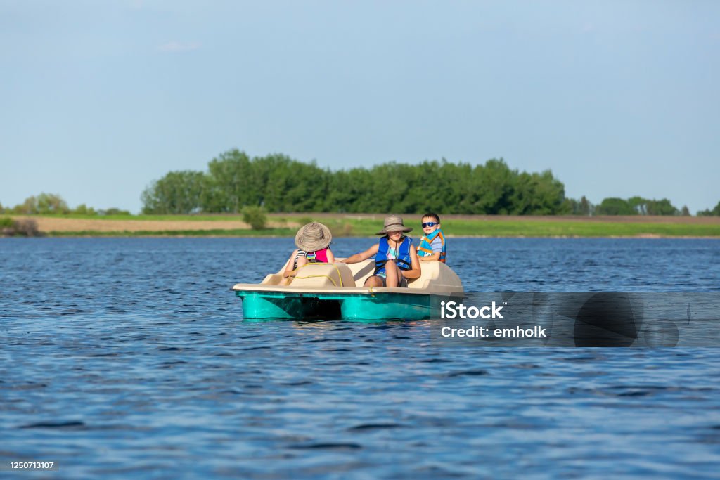 Three Children in Paddleboat on Lake Water Three young children (two sisters and their little brother) in a paddle boat on the lake on a beautiful summer day. Pedal Boat Stock Photo