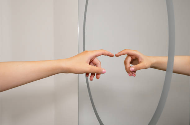 Photo of A caucasian woman's hand reflected in a clean bathroom mirror as she reaches out and almost touches. A representation a social distancing and hygiene concept.