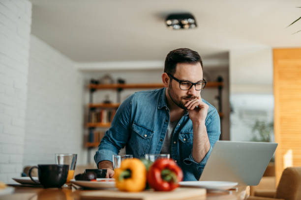 istock Pensive man at kitchen table looking for a cooking recipe on laptop. 1250720936