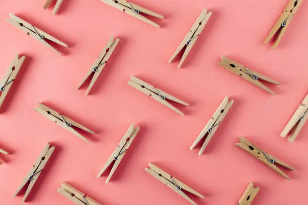 Wooden biodegradable clothespins repetitive pattern on abstract pastel pink background