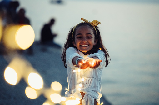 Happy kid on beach holiday holding fairy lights in hands and smiling to camera