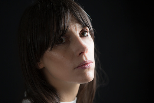 A portrait of a girl with bangs in front of a black background.  She is looking at the camera.  Half of her face is slightly shadowed.
