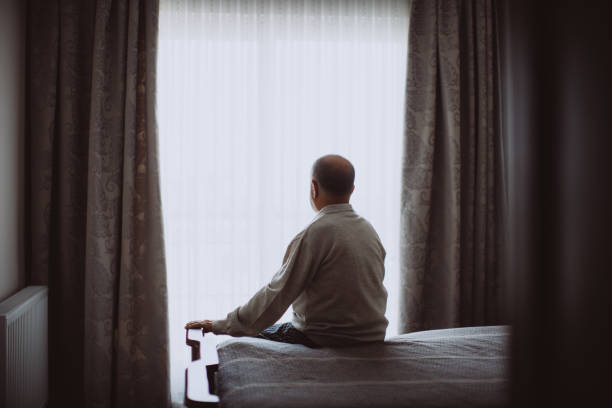 elderly man sitting on bed looking serious - loneliness solitude sadness depression imagens e fotografias de stock