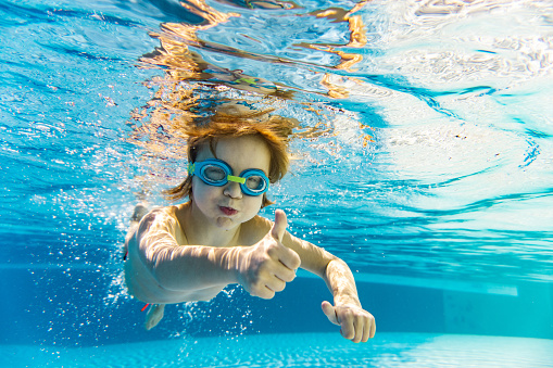 Smiling child is pointing a thumb up while he is underwater