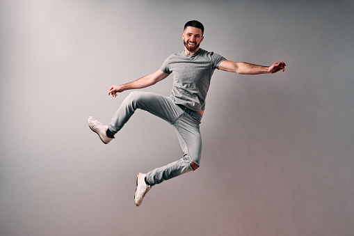 Concept of advertising, discounts, fun, clothing, lifestyle.Full length portrait of an excited handsome young man in gray t-shirt jumping while celebrating success isolated over gray background.