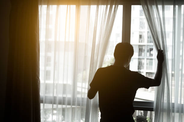 istock Man in dark room opens curtains on window to the morning light 1250837657