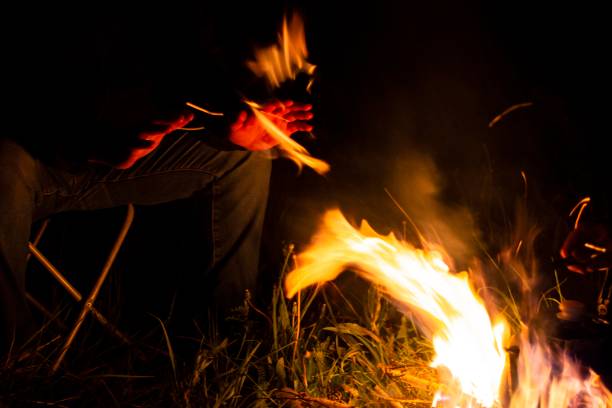 istock man sitting on a camping chair warming his hands by the fire on a dark night 1250902400