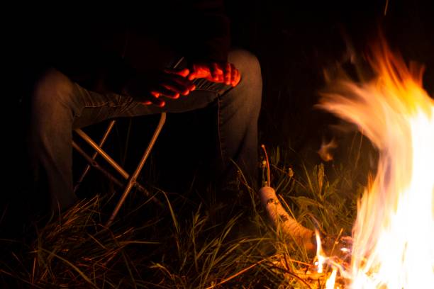 istock man sitting on a camping chair warming his hands by the fire on a dark night 1250902401