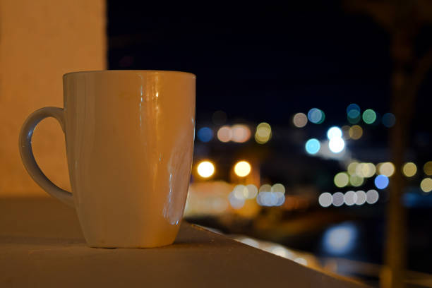 Romantic blurred image night cityscape as a background with white mug on the window.