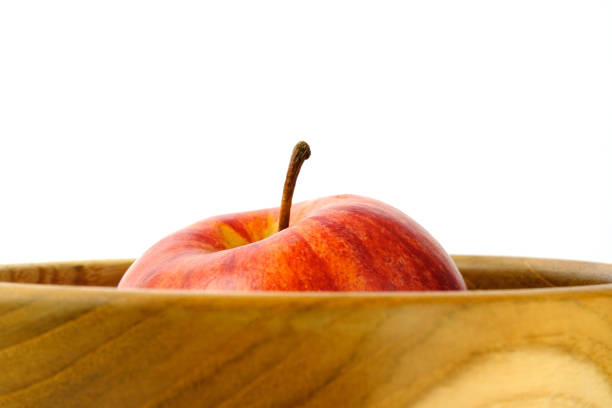 Close up single red Apple above wooden bowl / basket isolated on white background with studio lighting