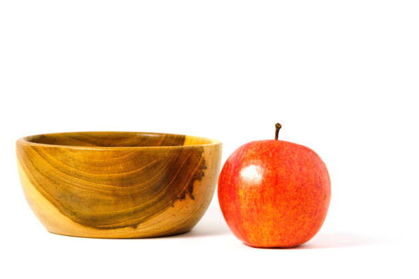 A red Apple fruit beside a wooden bowl / basket isolated on white background with studio lighting