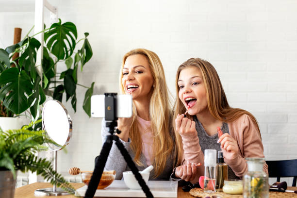 istock Mother and her daughter puting liquid lipstick on lips and record video about cosmetics on mobile phone 1250908444