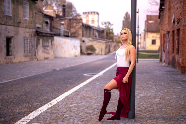Blonde young pretty girl dancer perform in empty street leaning on pole