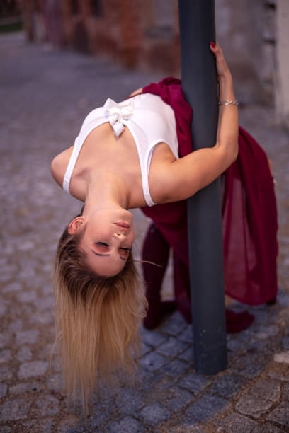 Blonde young pretty girl dancer perform in empty street leaning on pole