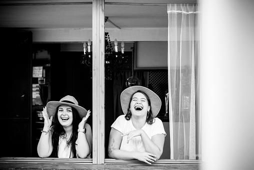 Happy young couple of girl friends enjoy the friendship and laugh a lot together at the window - people and fun life concept
