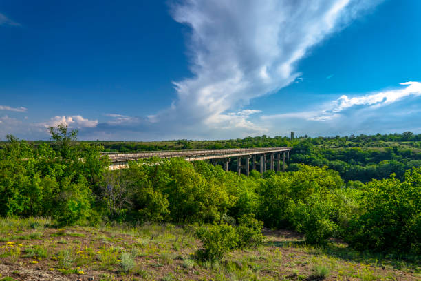 Ancient old bridge over Southern Bug. Yuzhny Buh river flow through green trees. Nature landscape