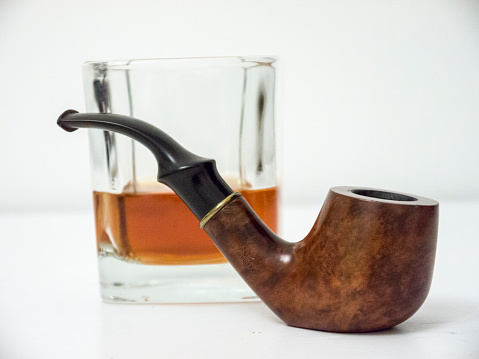 Briar brown smoking pipe with old fashioned glass of whisky close side view with distorted background color image