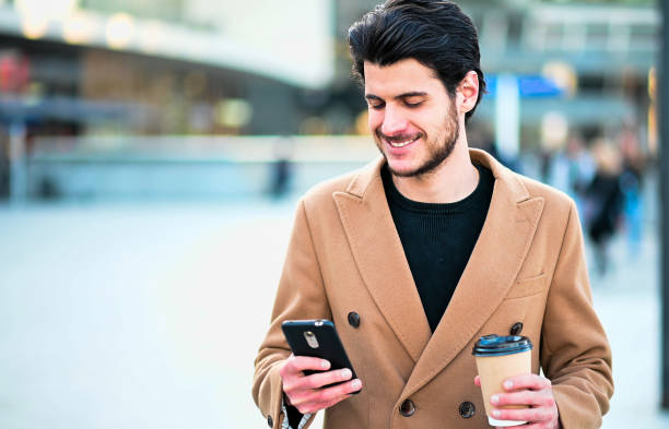 istock Handsome elegant dressed man using his smartphone and holding a cup of coffee 1250924054
