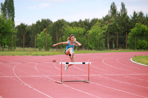 Female athlete jumping above the hurdle during the race.