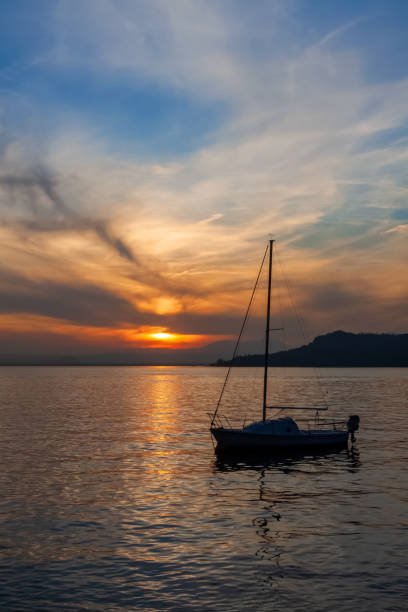 парусник на спокойном озере гарда с красочным закатом - lake garda sunset blue nautical vessel стоковые фото и изображения