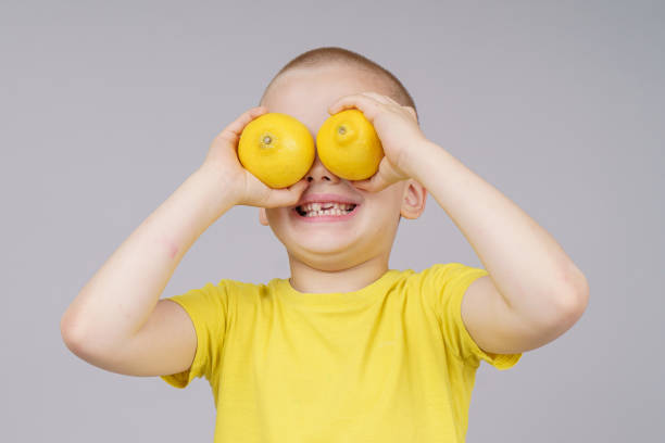 istock Smiling boy standing with fruit, holds lemon instead of eyes. Isolated on gray 1250935847
