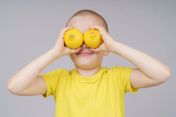 istock Smiling boy standing with fruit, holds lemon instead of eyes. Isolated on gray 1250935848