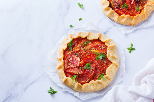 Small savoury homemade vegetarian tomato galette, tart, seasonal summer open pie with aromatic herbs. Healthy and tasty bakery product, dessert with ripe fruits.