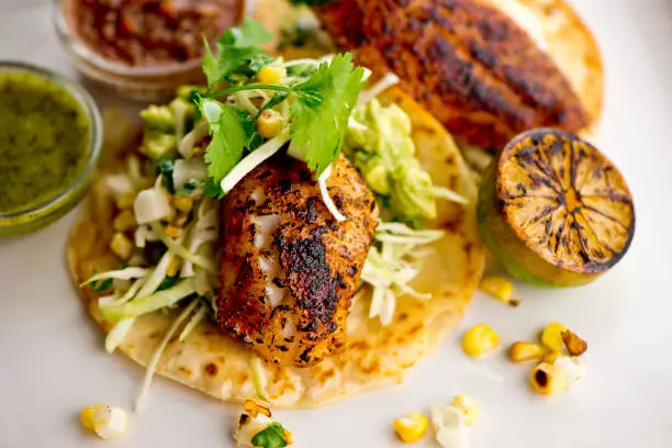 Fish tacos served on homemade corn tortilla with shredded cabbage, grilled corn, queso Fresca, jalapeños served with cilantro, guacamole and spicy salsa verde. Classic Mexican or Tex-Mex street food favorite.