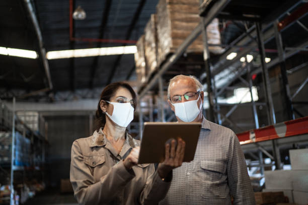 Senior partners walking and using digital tablet at warehouse - with face mask Senior partners walking and using digital tablet at warehouse - with face mask checklist photos stock pictures, royalty-free photos & images