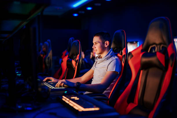 Smiling young professional gamer playing video game at internet cafe or playroom, portrait. Smiling young professional gamer playing video game at internet cafe or playroom, portrait. gaming chair photos stock pictures, royalty-free photos & images