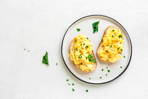 Scrambled Eggs on toasts for healthy breakfast or brunch, top view, copy space. Homemade  meal - scrambled eggs sandwiches.